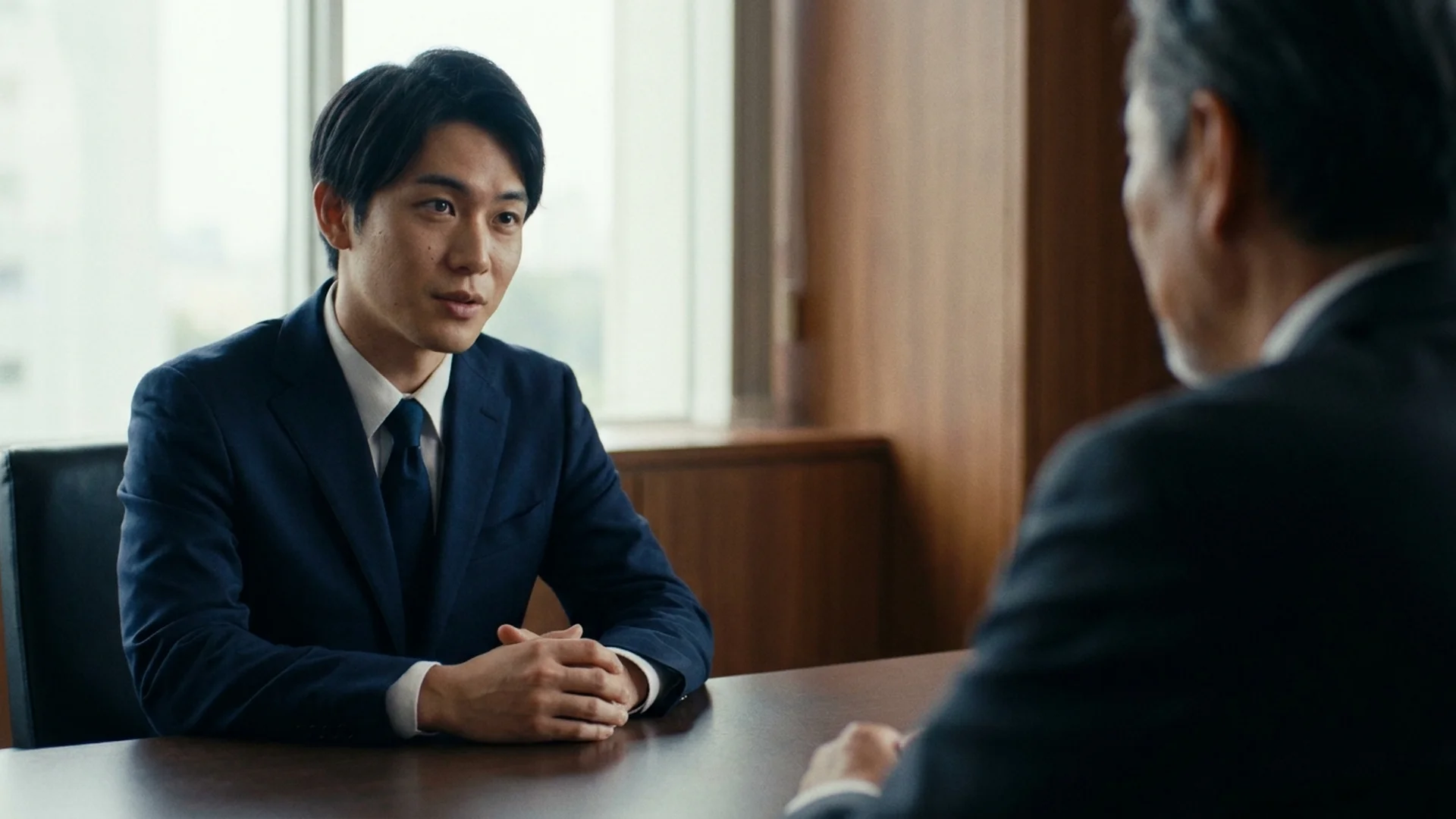 A young Japanese office worker listening to a senior colleague in a meeting room