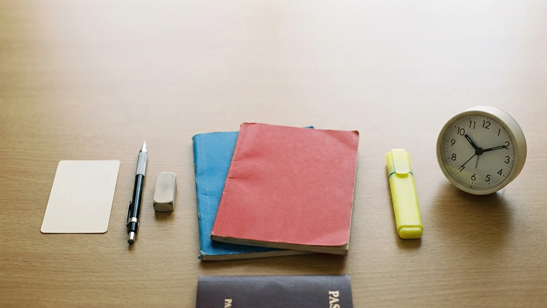 A study desk with exam workbooks, a blank admission-ticket-style card, a clock, and a passport