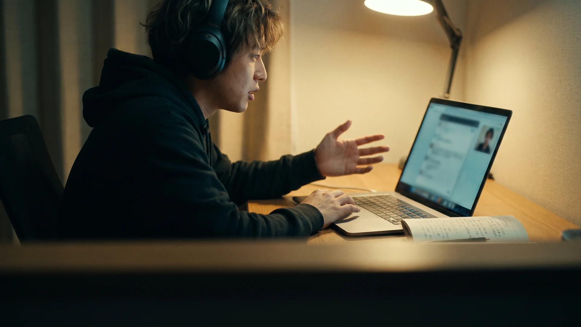 A person wearing headphones gesturing while speaking during a video call lesson at a home desk